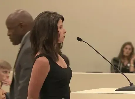 A woman stands in front of a microphone in a courtroom