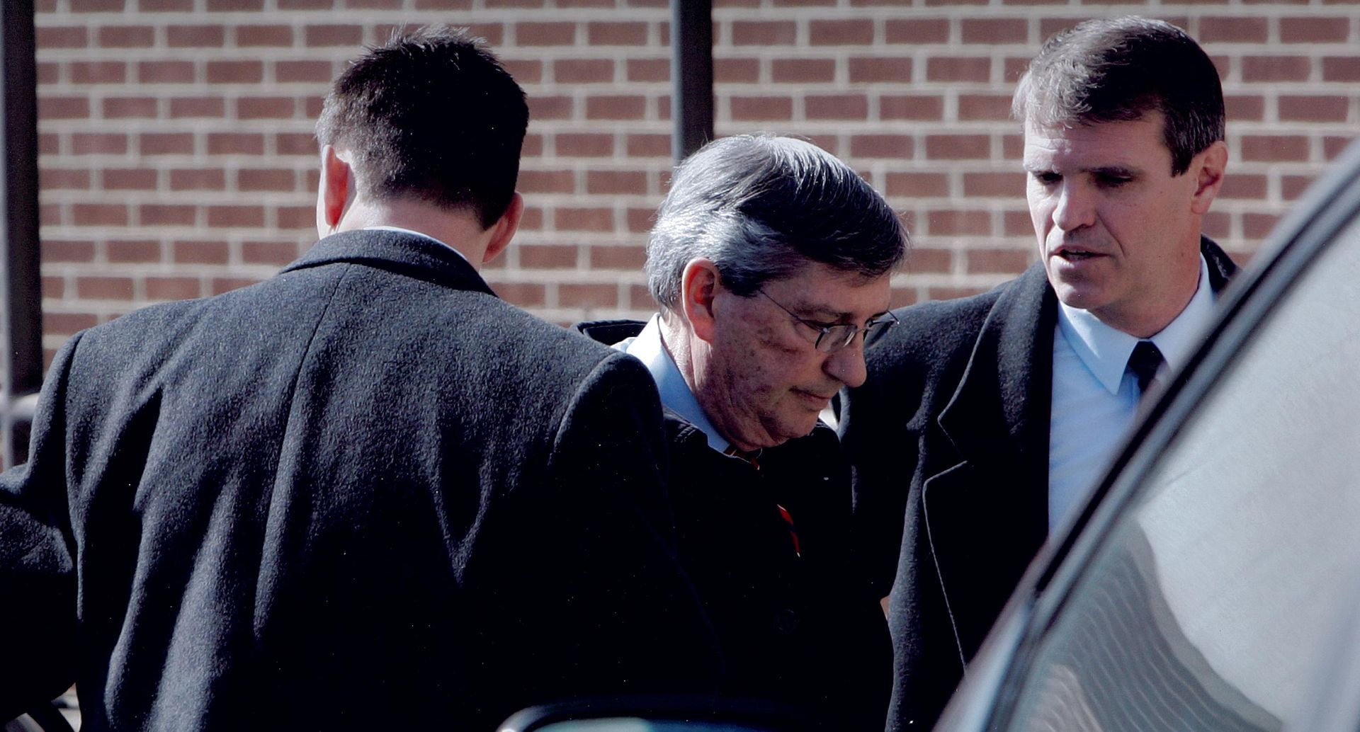 A group of men are standing around a car talking to each other.