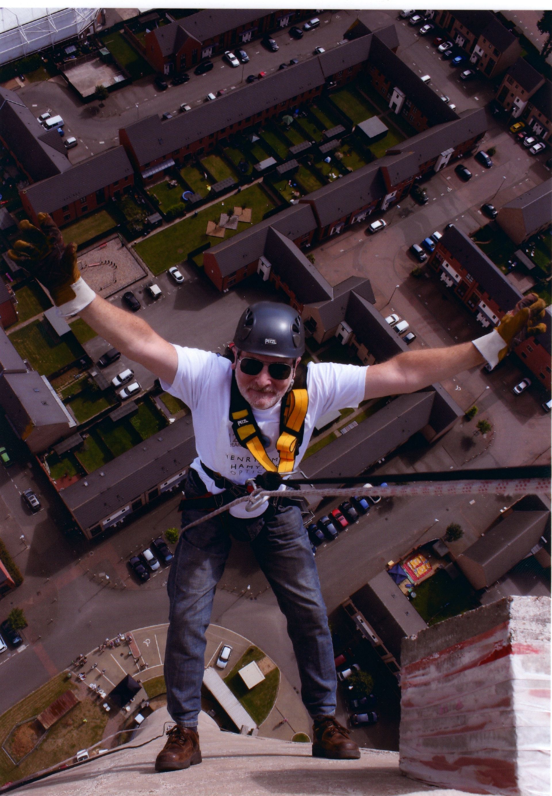 Tony, in a helmet and white t-shirt, spreads his arms wide while abseiling