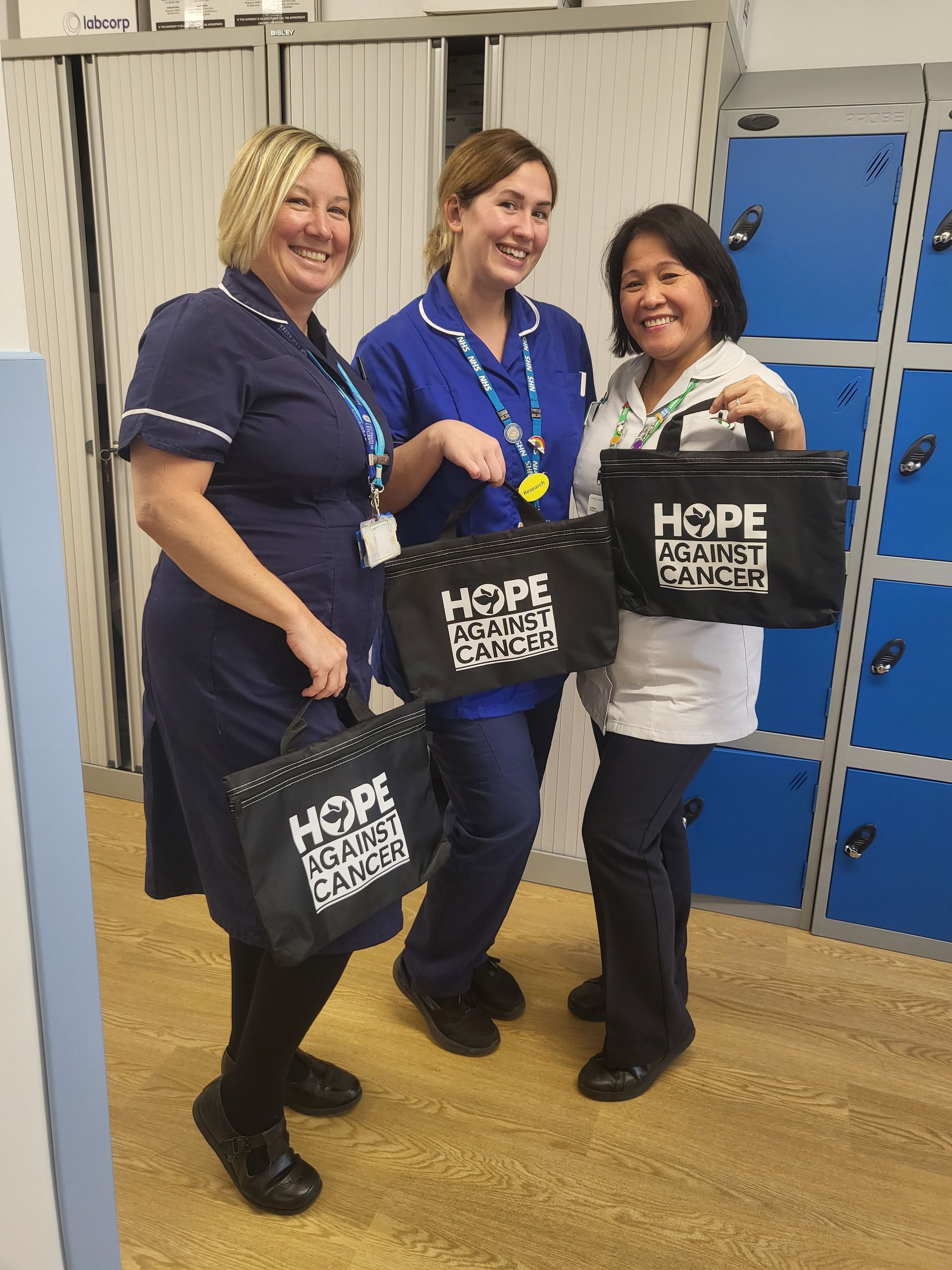 Three women standing next to each other holding bags that say hope