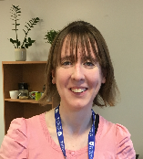 A woman in a pink shirt and blue lanyard is smiling for the camera.