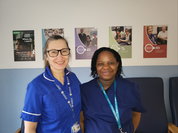 Two nurses are posing for a picture in front of posters on the wall