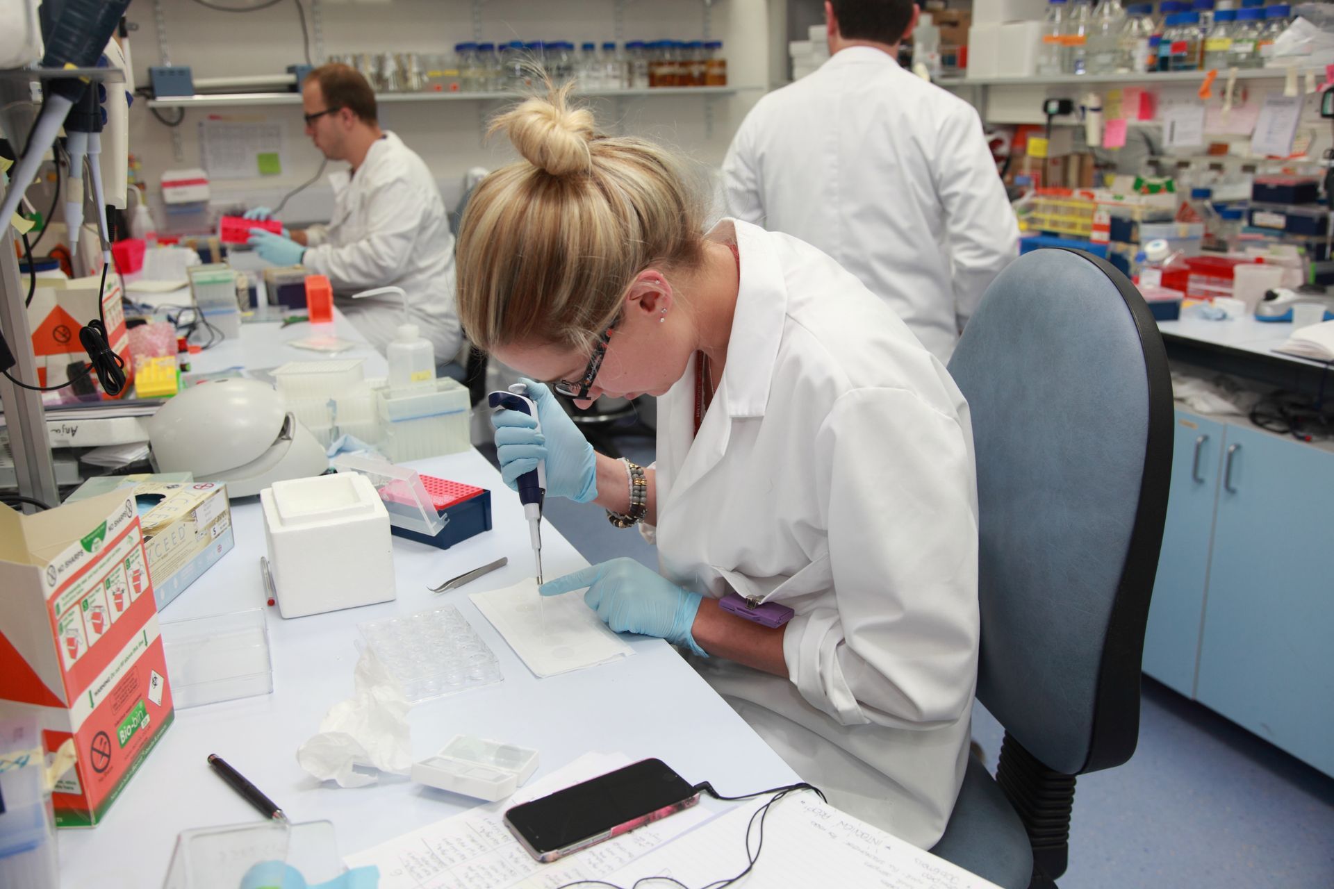 A woman in a lab coat is working on a cell phone