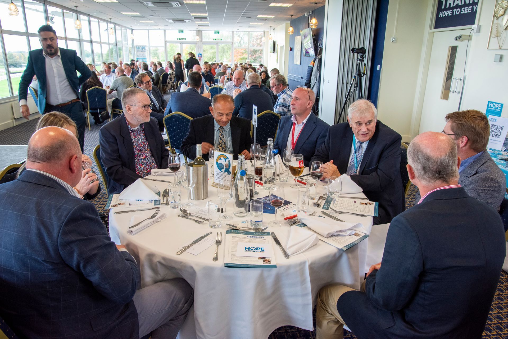 A group of people are sitting at tables in a room with a sign that says hope against cancer.