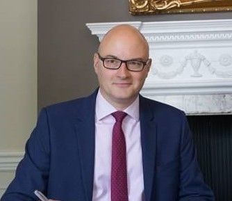 A man in a suit and tie is sitting in front of a fireplace.