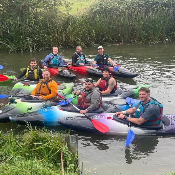 A group of people are sitting in kayaks on a river.