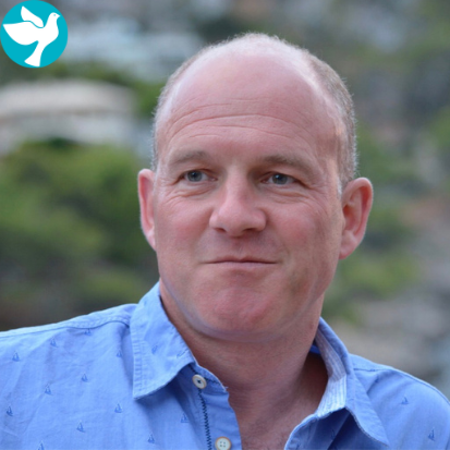 A bald man wearing a blue shirt is looking at the camera