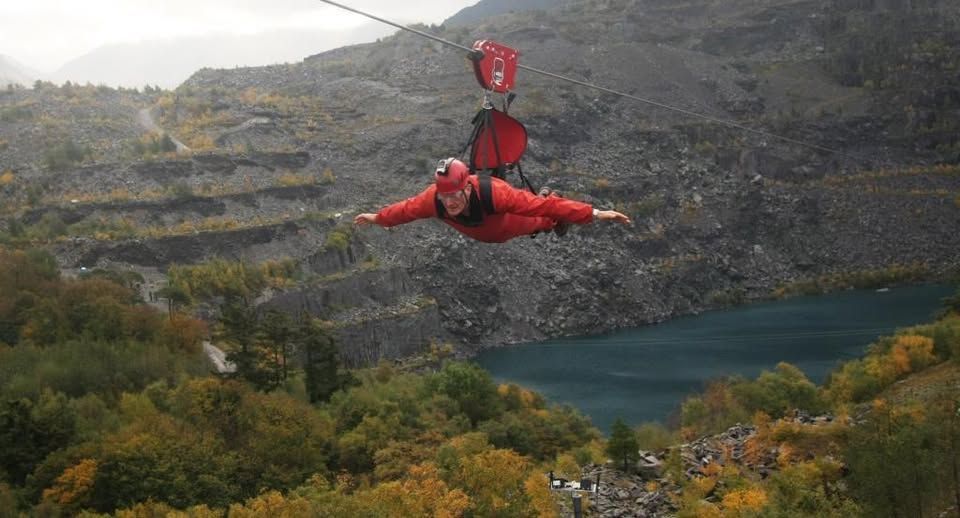 Tony on a zip wire in Snowdonia. He is strapped into a full red body suit