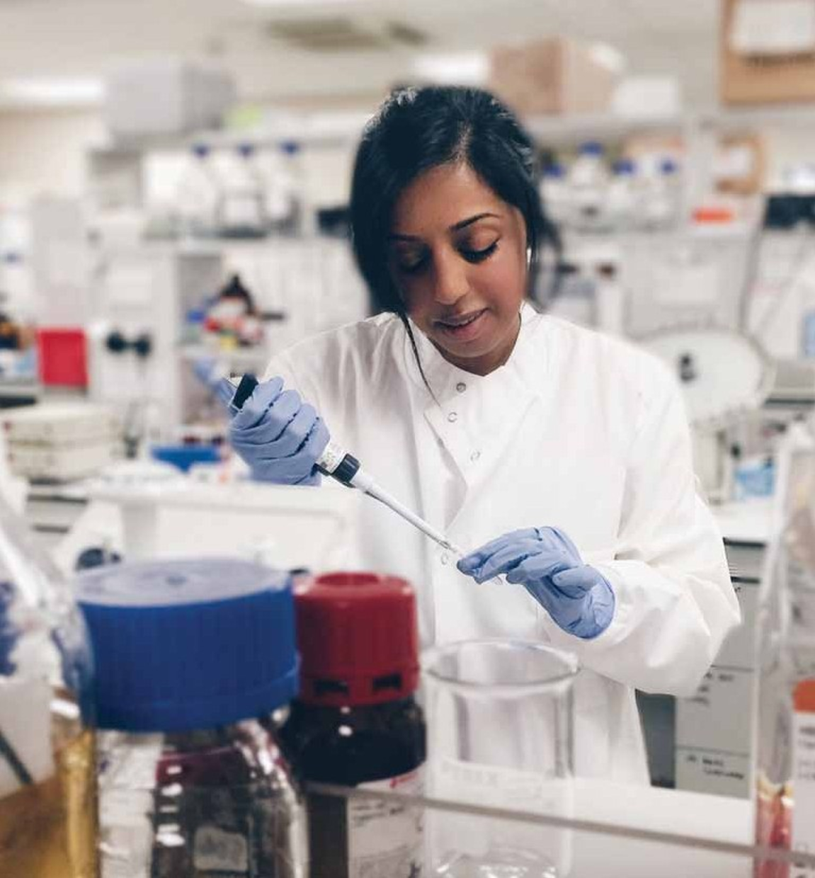 A woman in a lab coat is pouring liquid into a glass