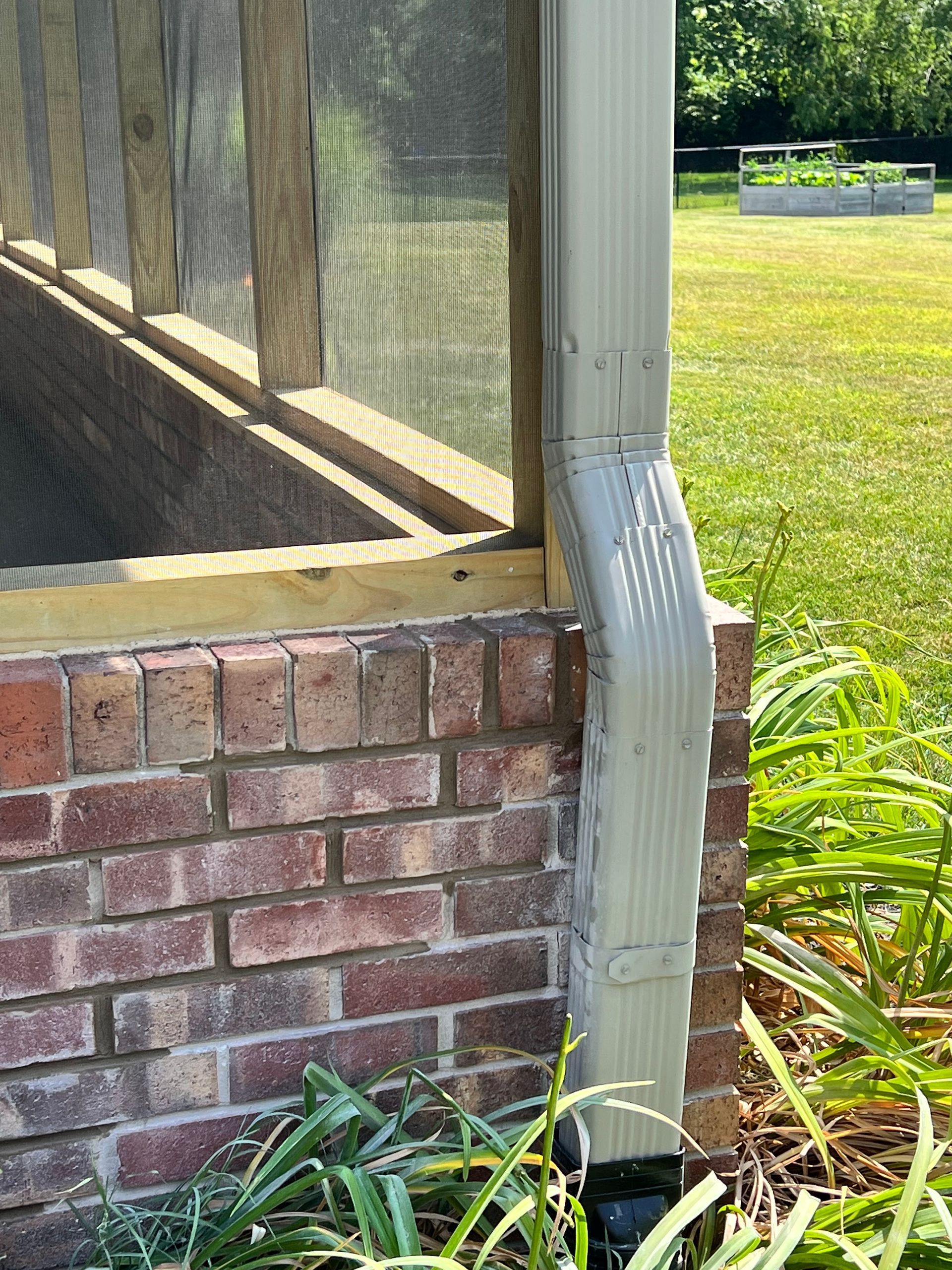 A brick wall with a screened in porch and a drain pipe.