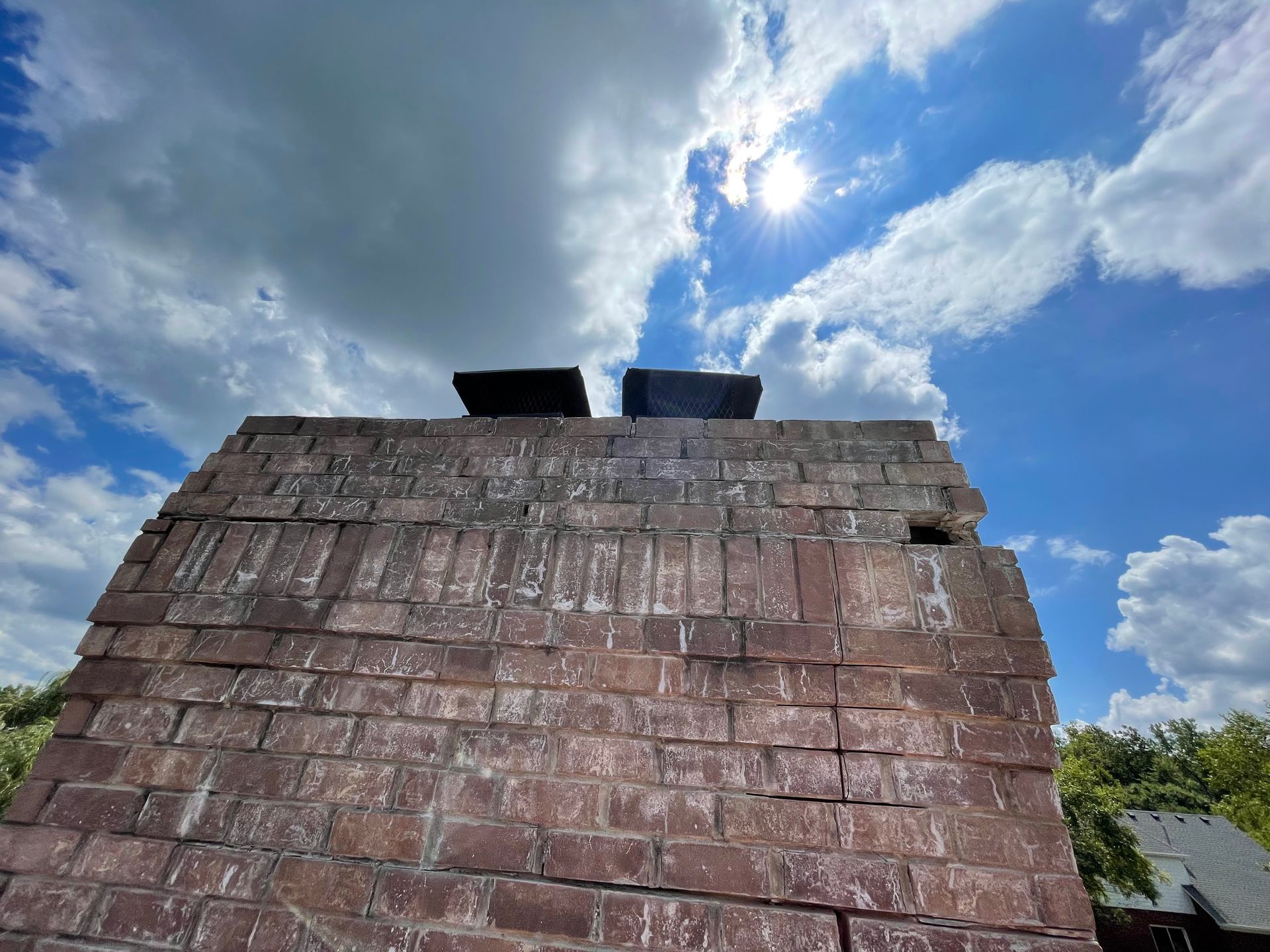 The sun is shining through the clouds over a brick chimney.