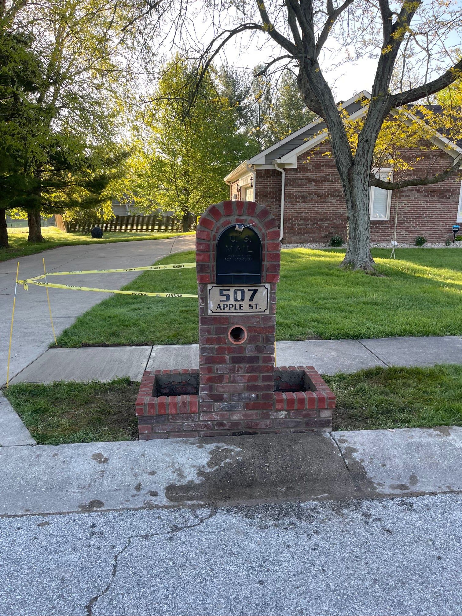 A brick mailbox is sitting on the sidewalk in front of a brick house.