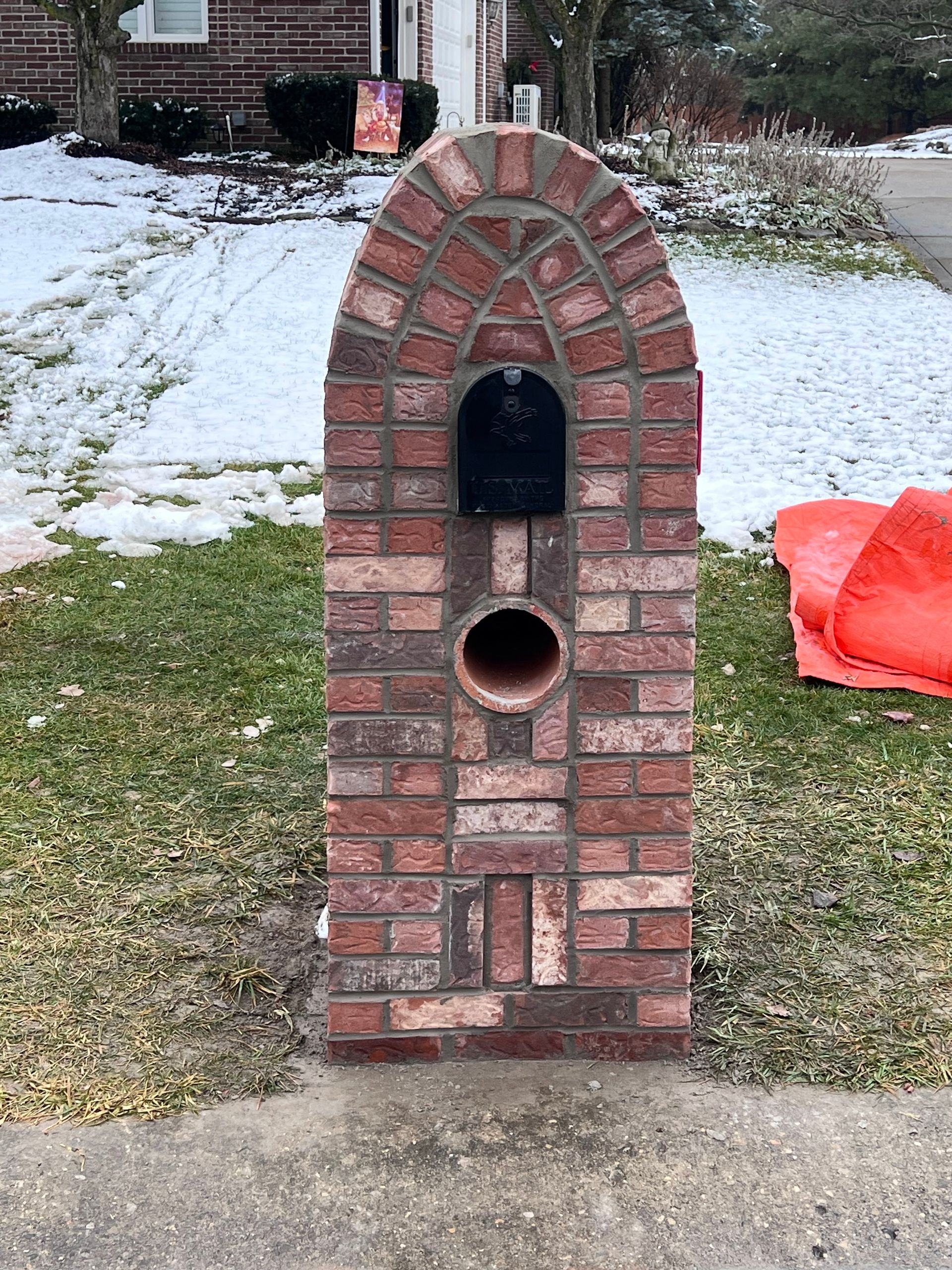 A brick mailbox is sitting in the grass in front of a house.
