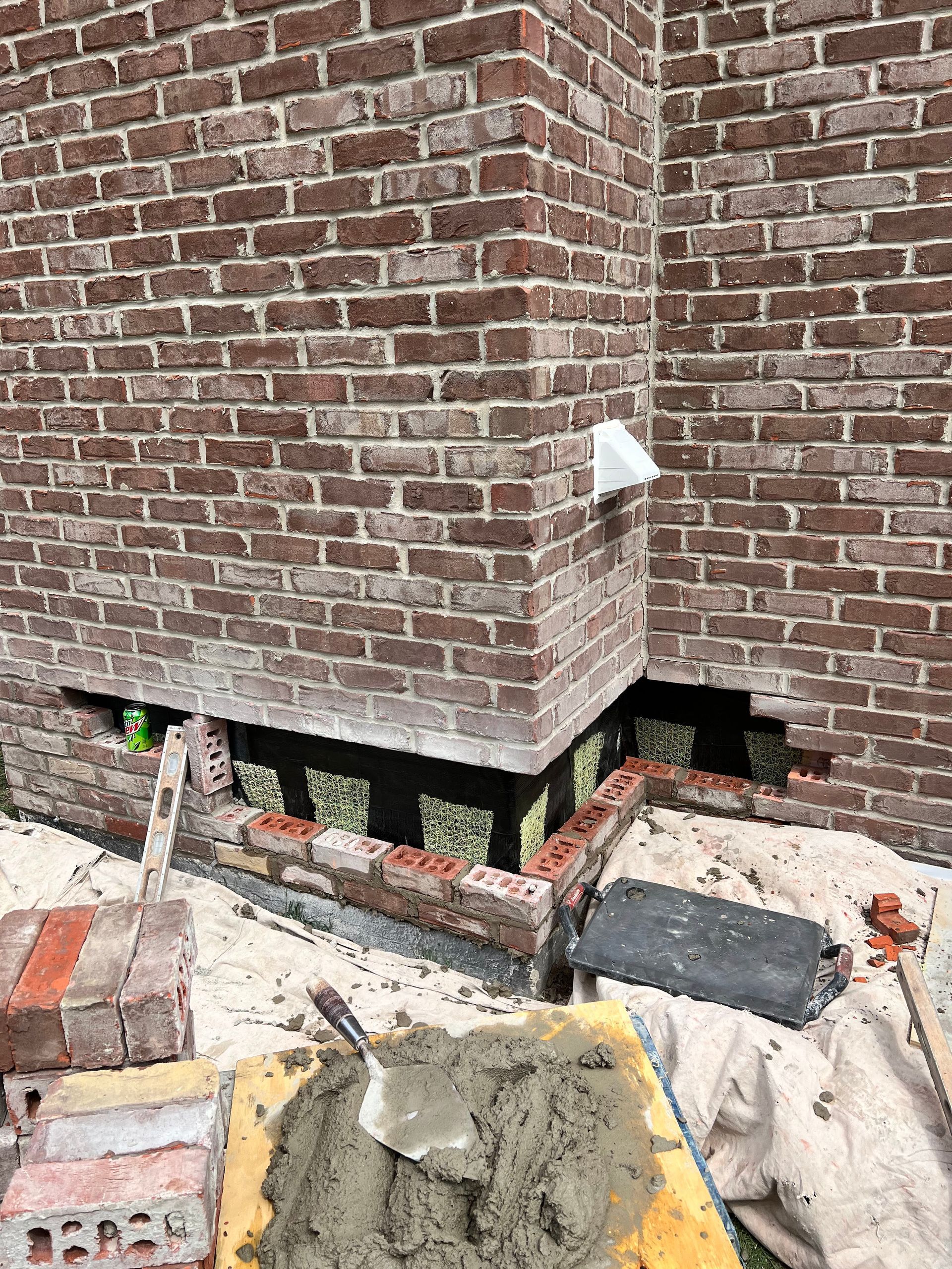 A brick wall with a hole in it and a wheelbarrow filled with cement.