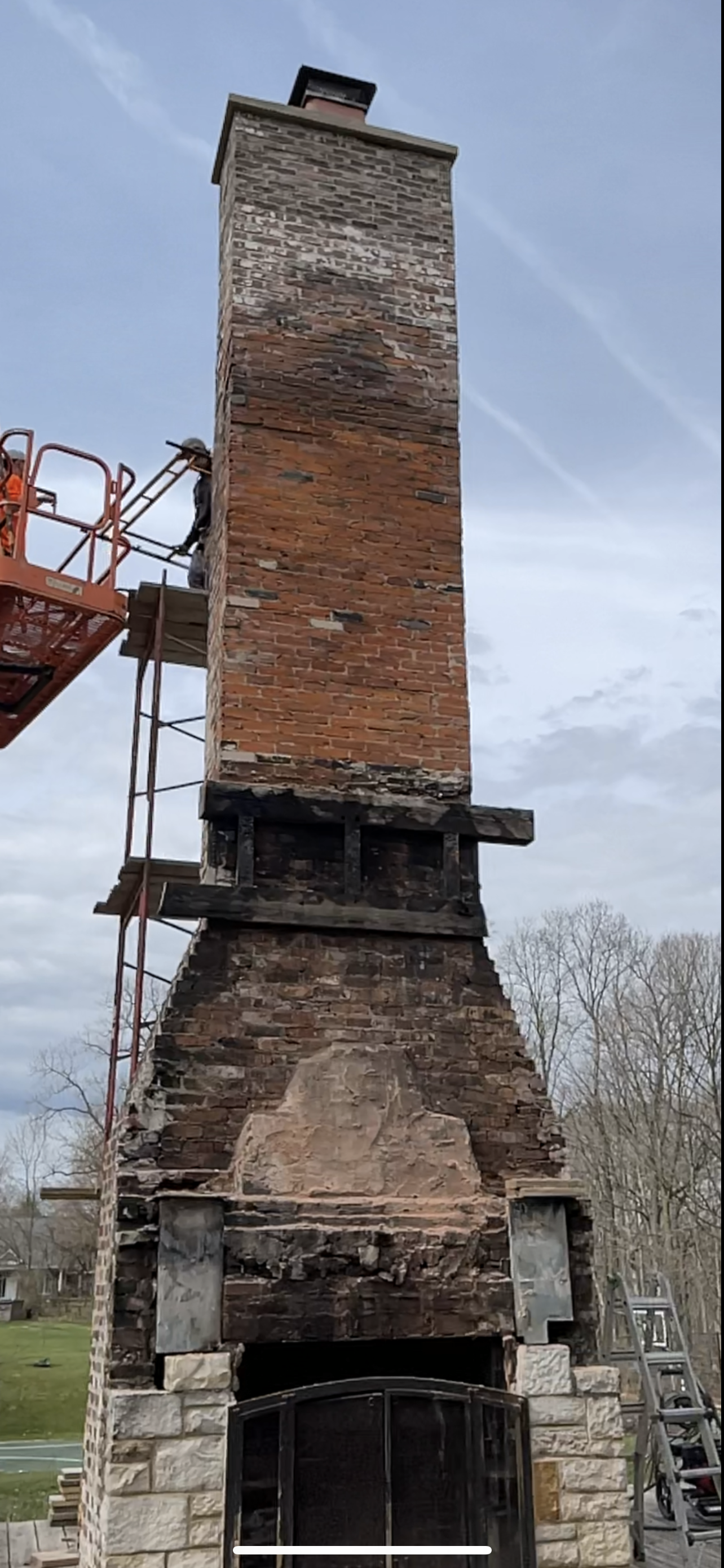 A large brick chimney is being repaired by a crane.