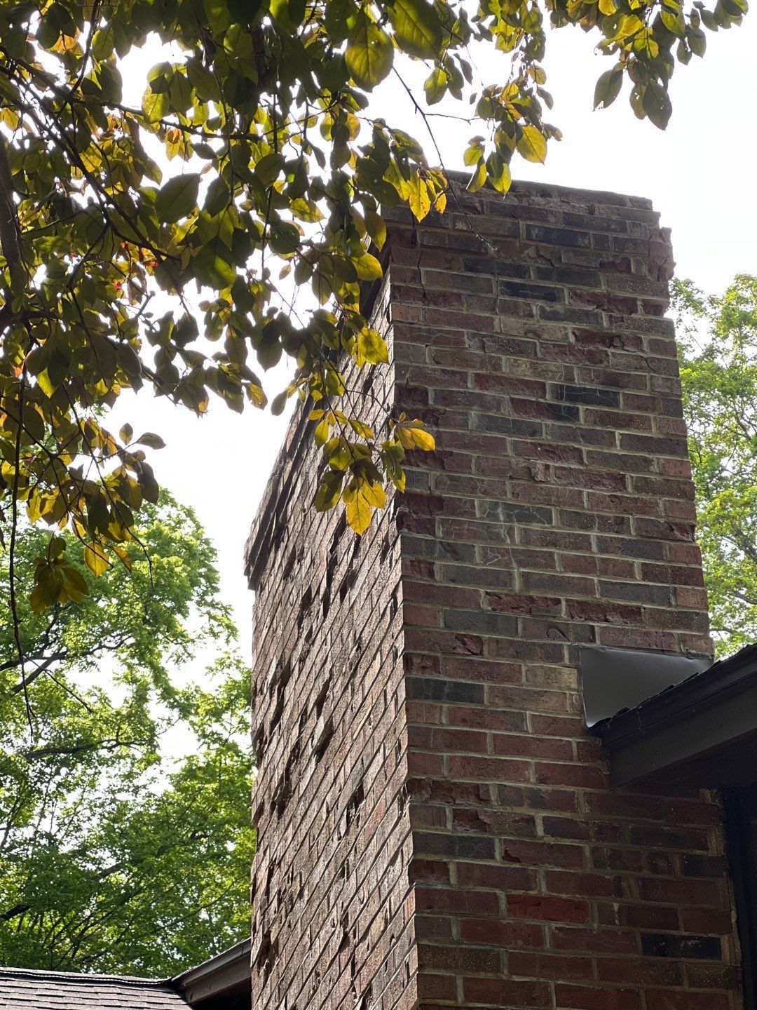 A brick chimney is surrounded by trees and a roof.
