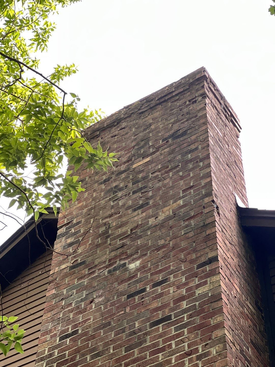 A brick chimney on the side of a house with trees in the background.