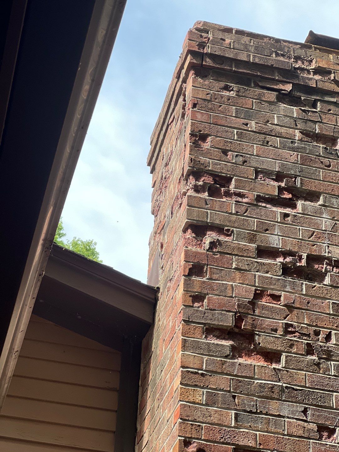 A brick chimney with holes in it is next to a house.