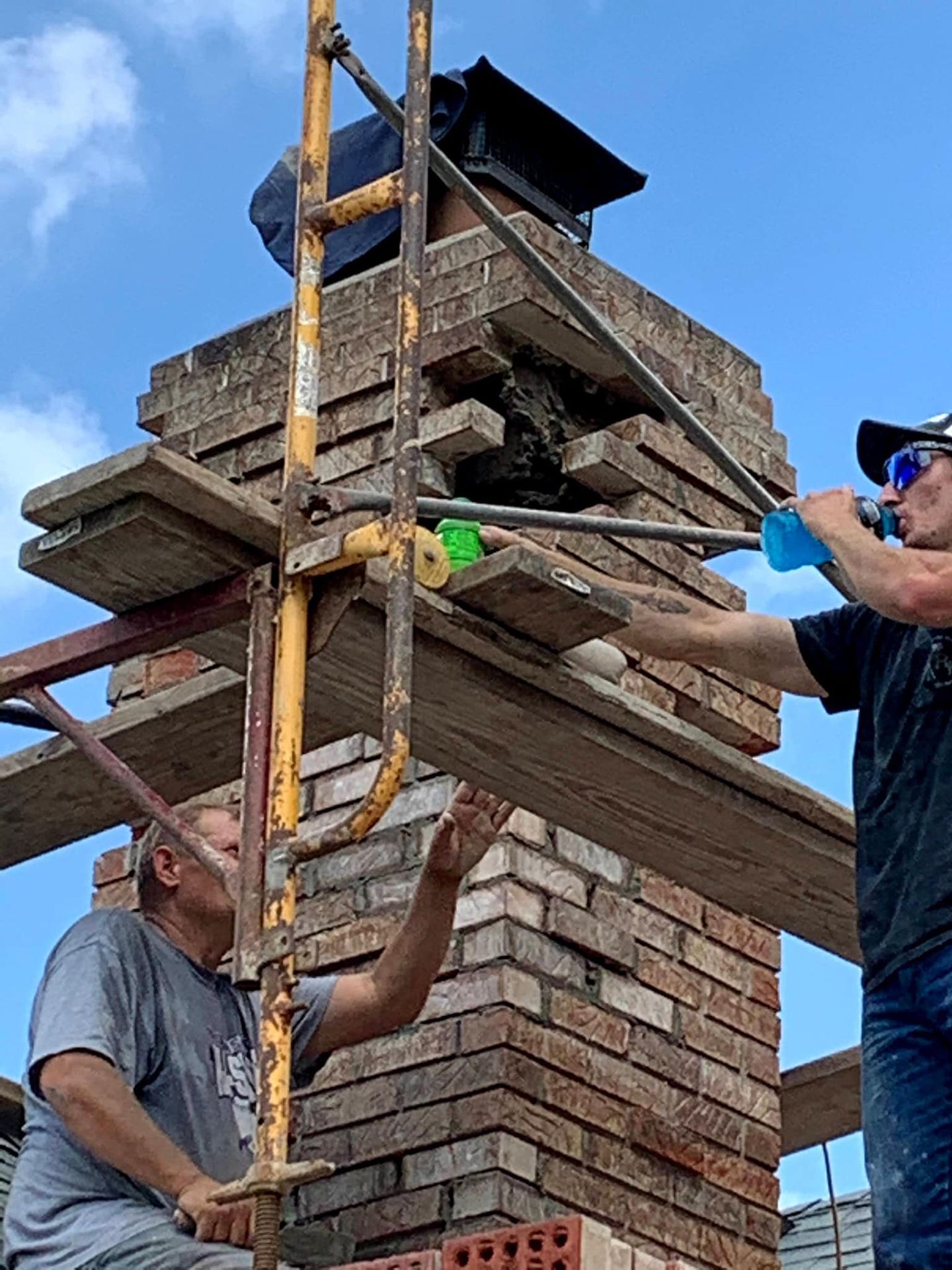 Two men are working on a brick chimney on a scaffolding.