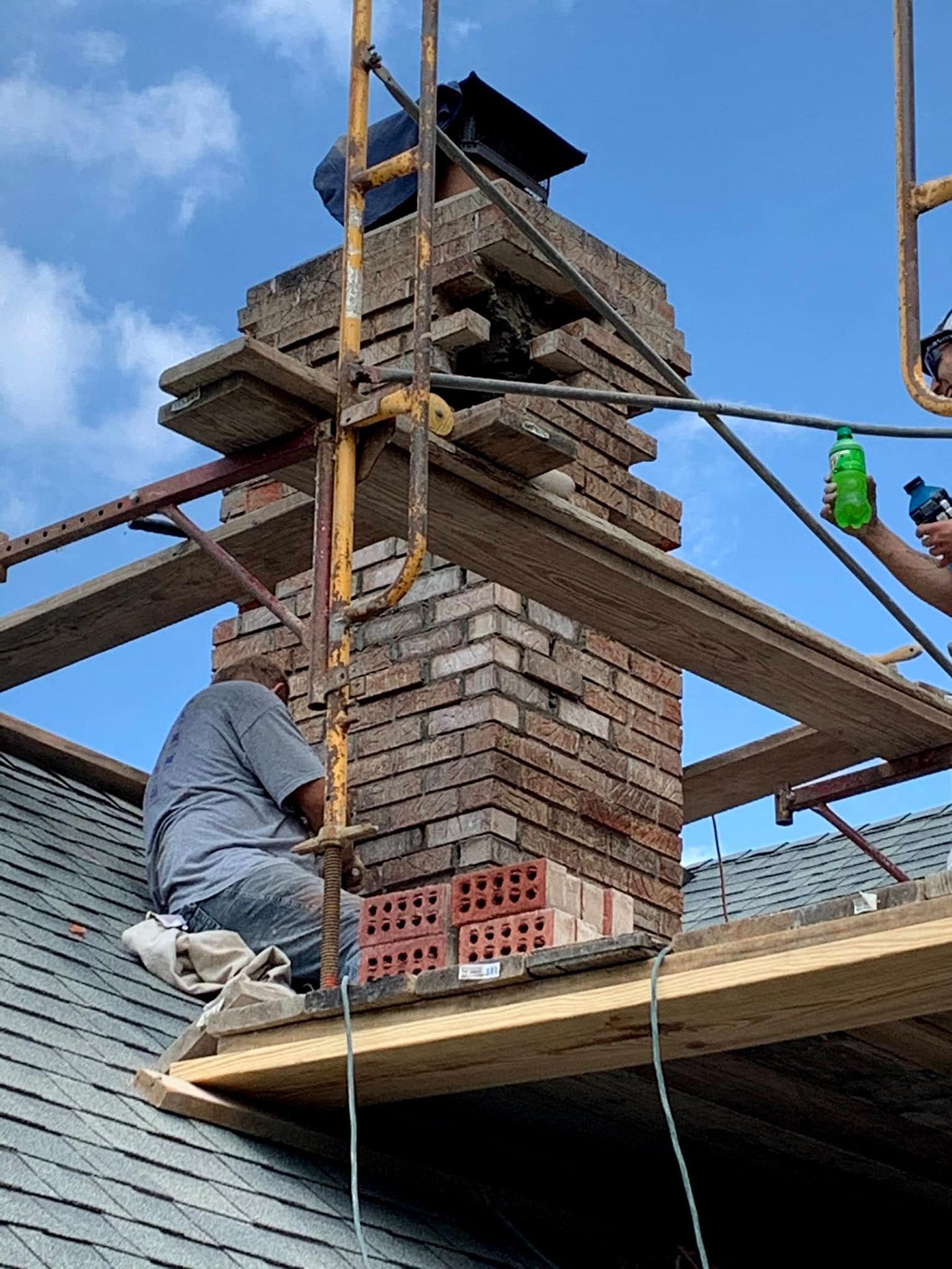A man is working on a brick chimney on the roof of a house.