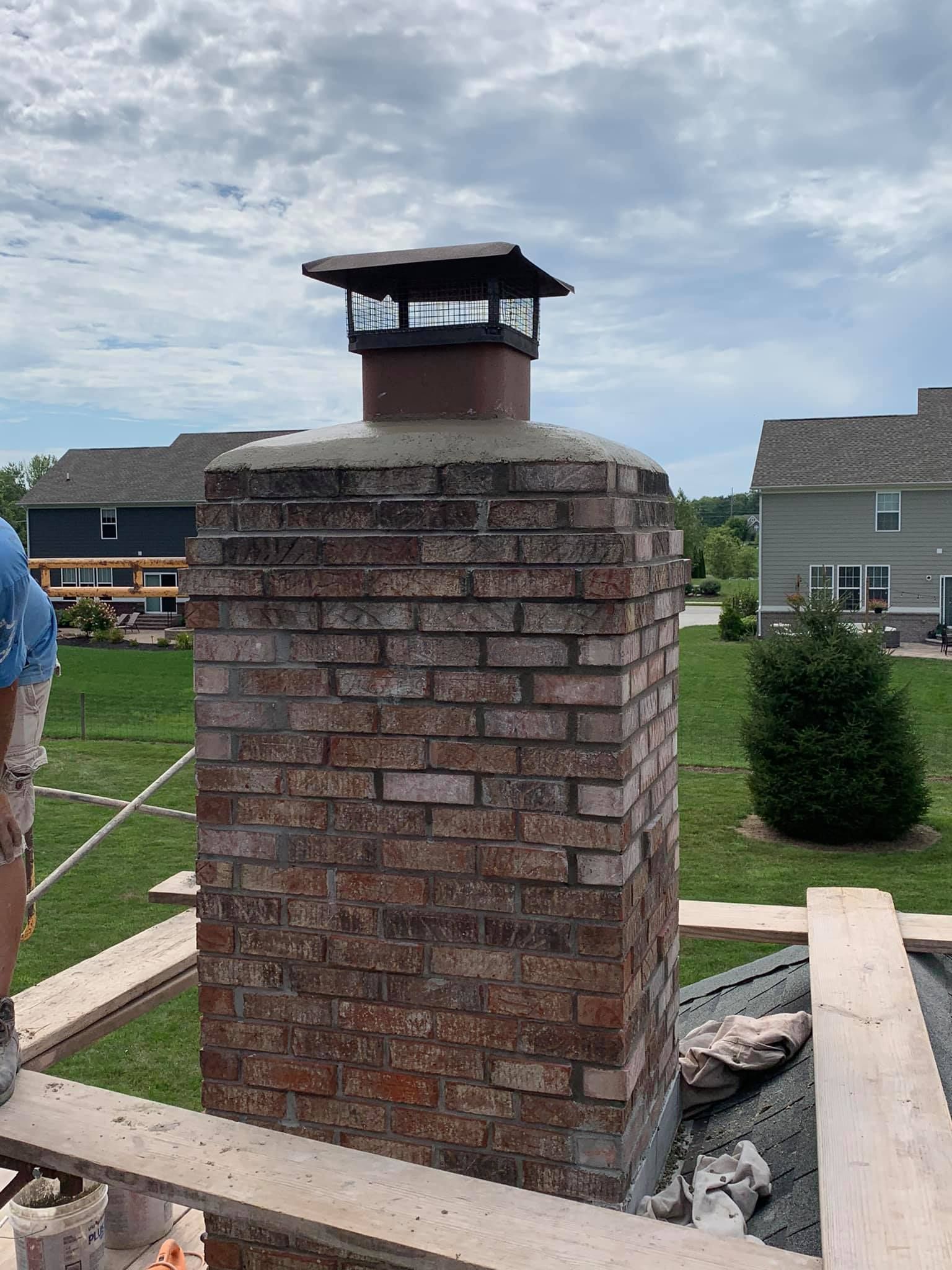 A brick chimney is sitting on top of a brick wall in a yard.