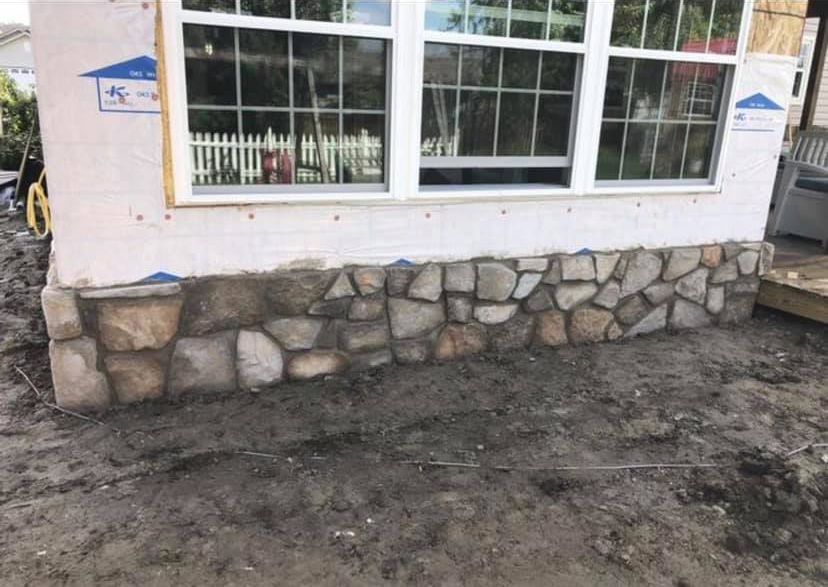 A stone wall is being built on the side of a house next to a window.