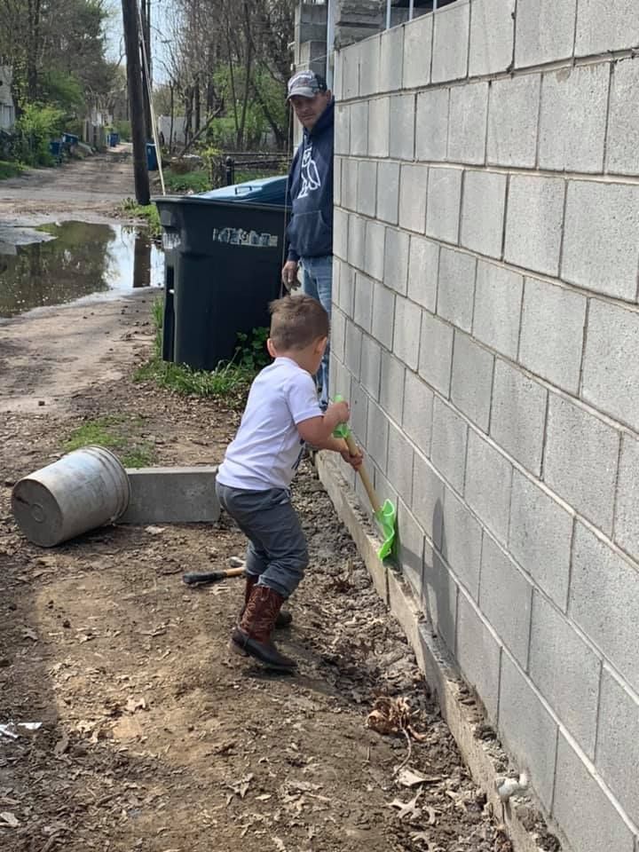 A little boy is standing next to a brick wall holding a broom.