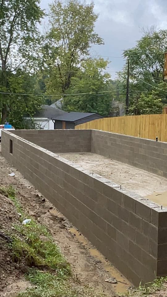 A large brick wall is being built around a swimming pool.