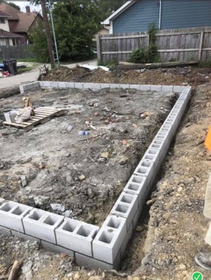 A concrete block wall is being built in the dirt in front of a house.
