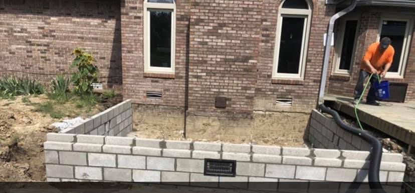 A brick wall is being built in front of a brick house.