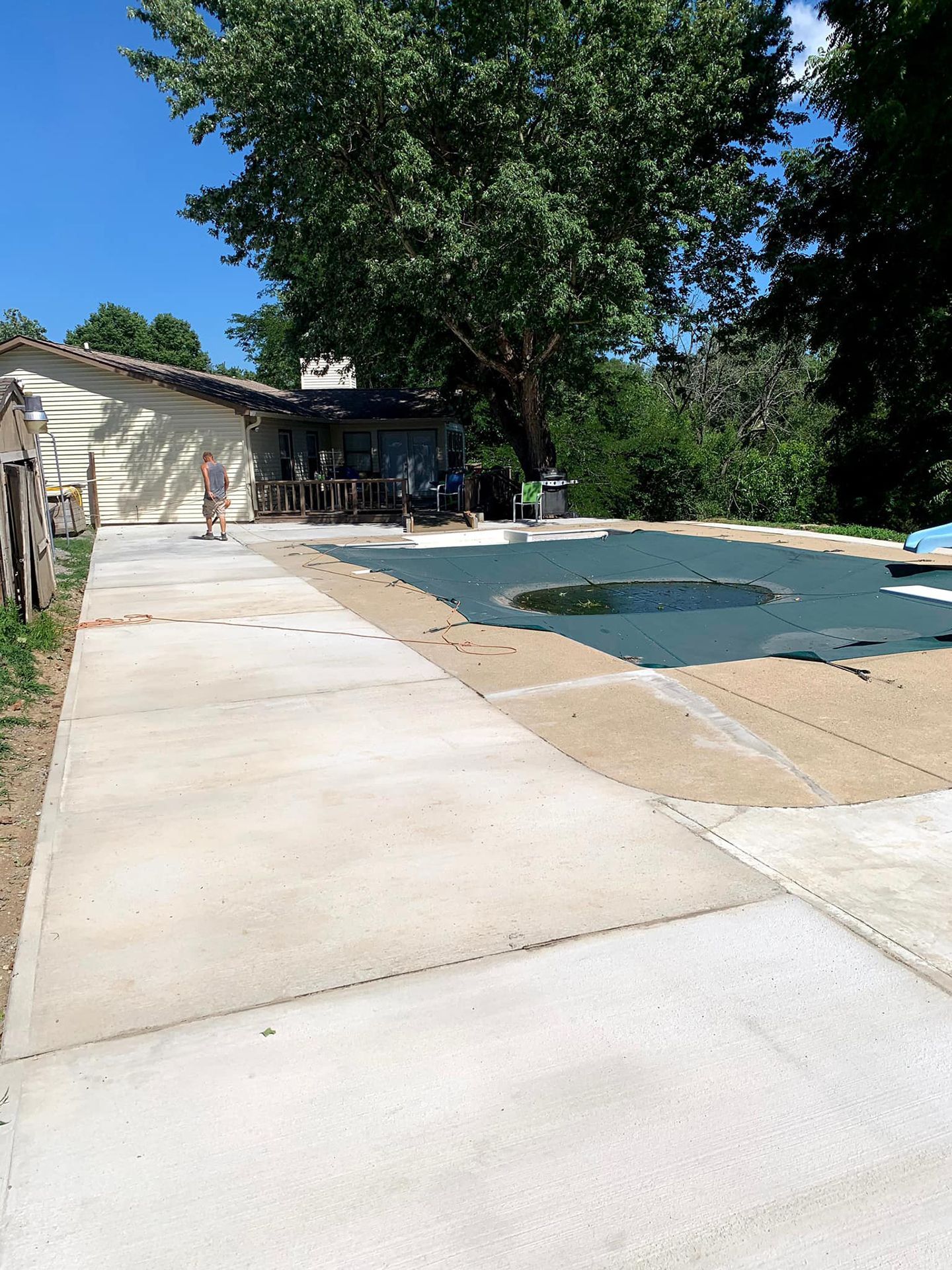 A concrete driveway leading to a swimming pool with a house in the background.