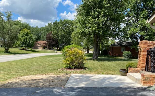 A driveway leading to a house in a residential neighborhood with trees and bushes.