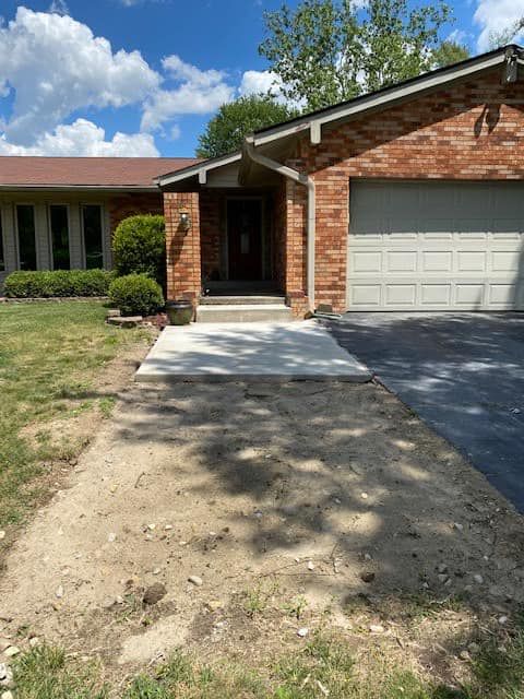 A brick house with a driveway and a concrete walkway in front of it.