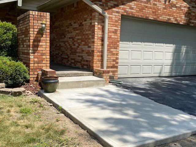 A brick house with a white garage door and a concrete walkway leading to it.