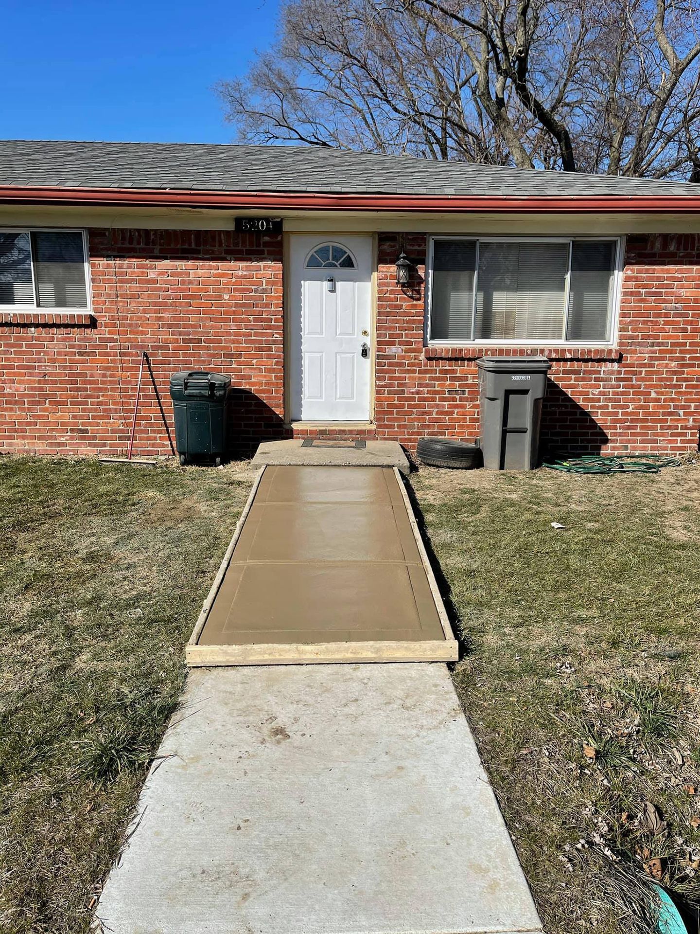 A brick house with a concrete walkway leading to the front door.