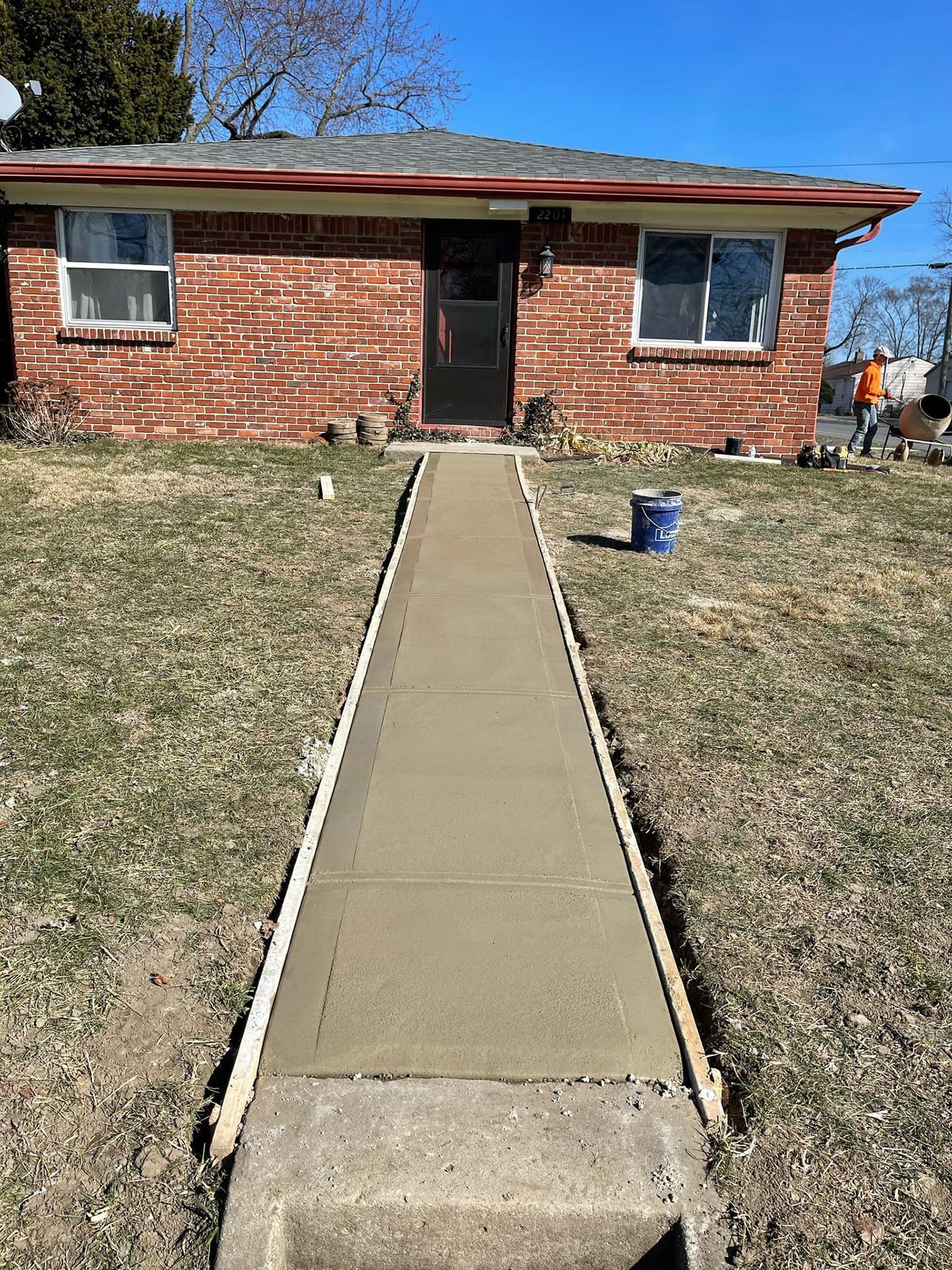 A concrete walkway is being built in front of a brick house.