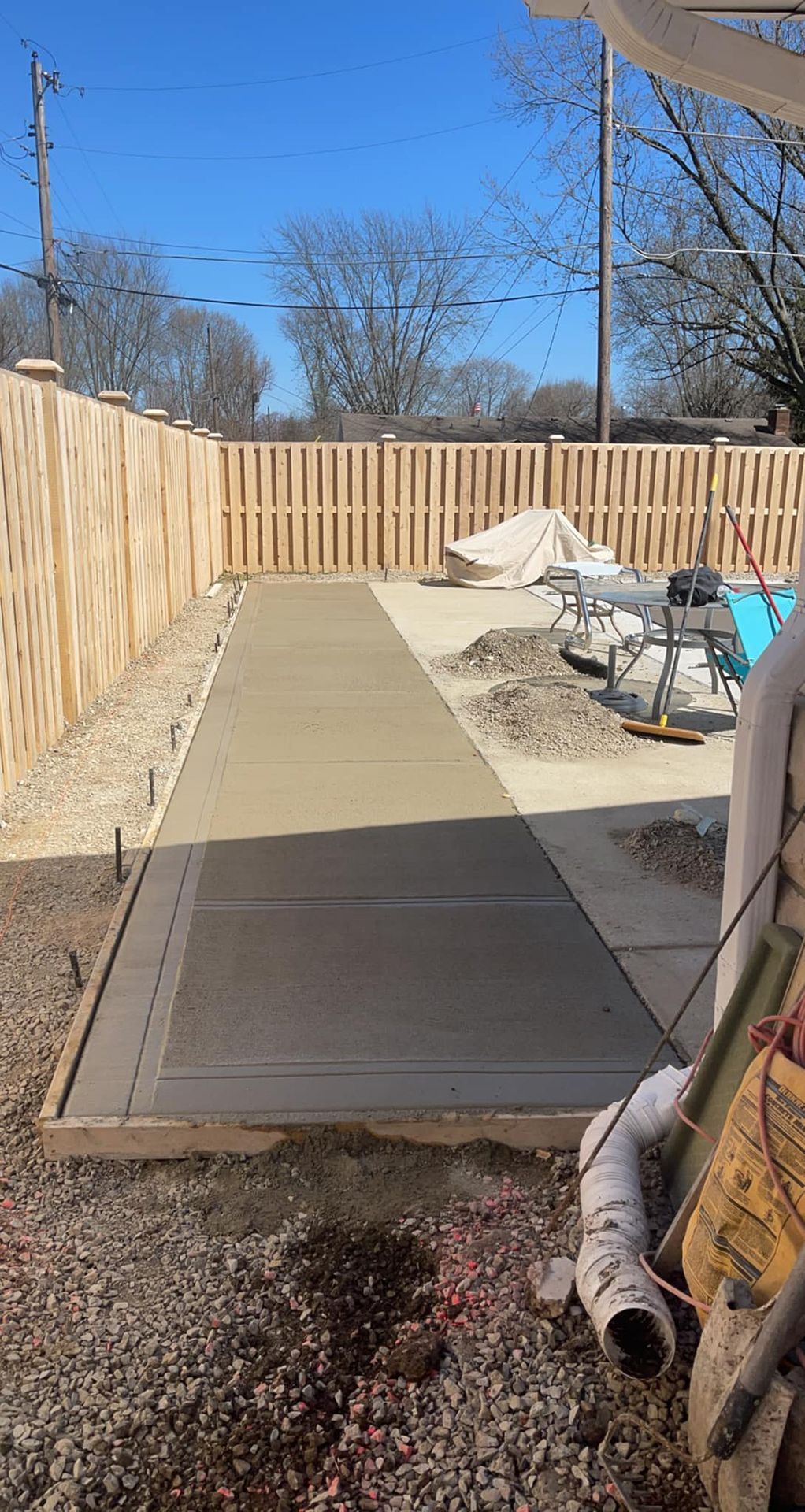 A concrete walkway is being built in a backyard next to a wooden fence.
