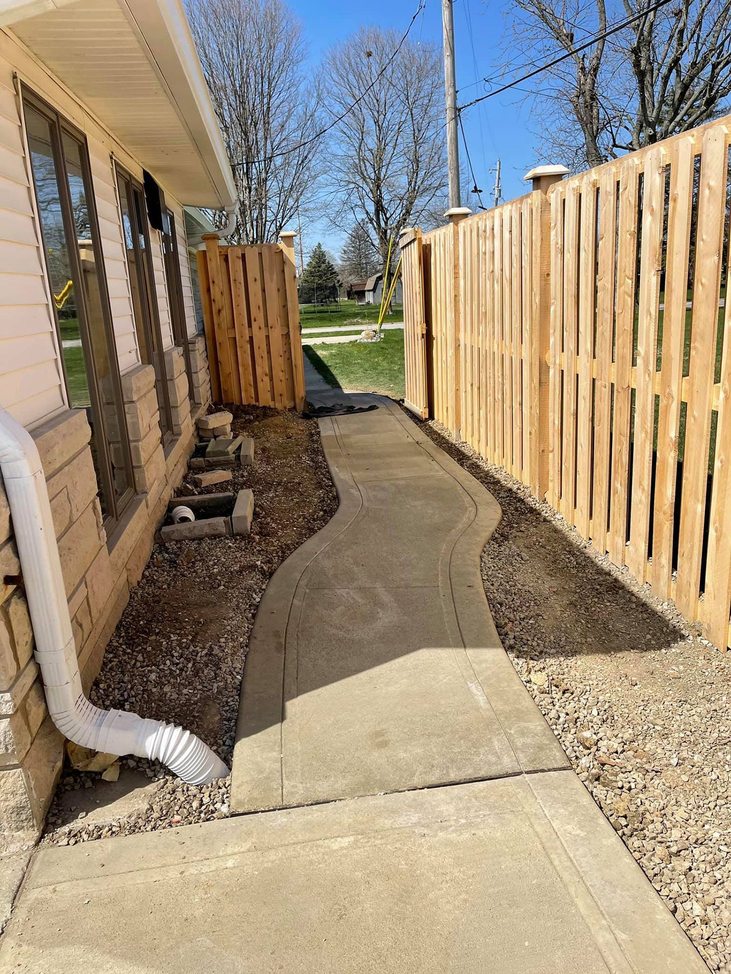 A concrete walkway leading to a wooden fence next to a house.