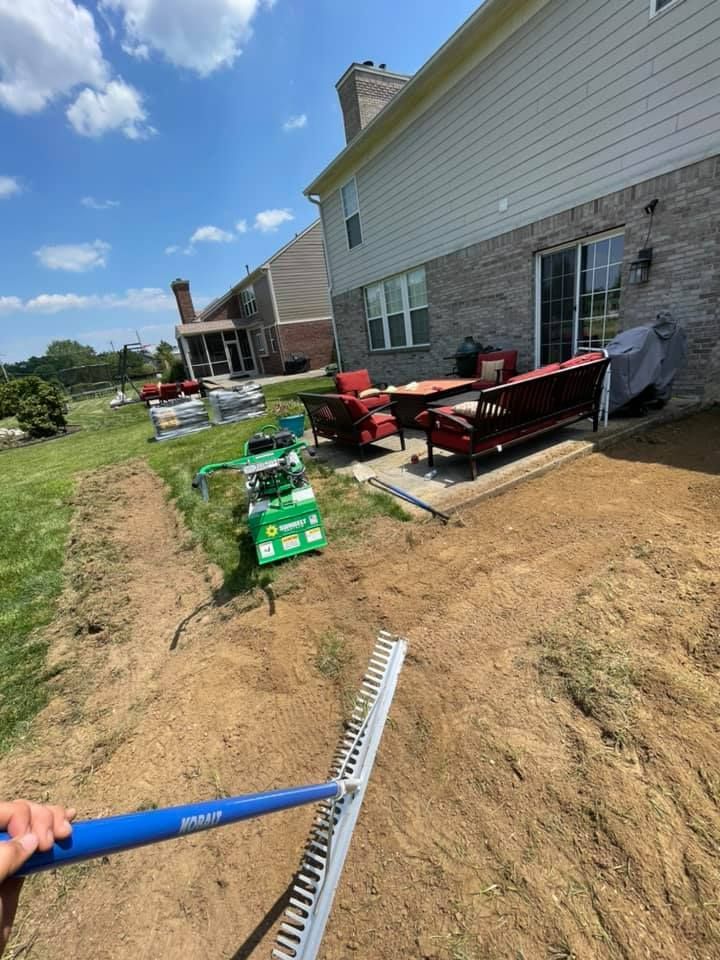 A person is raking dirt in a backyard in front of a house.