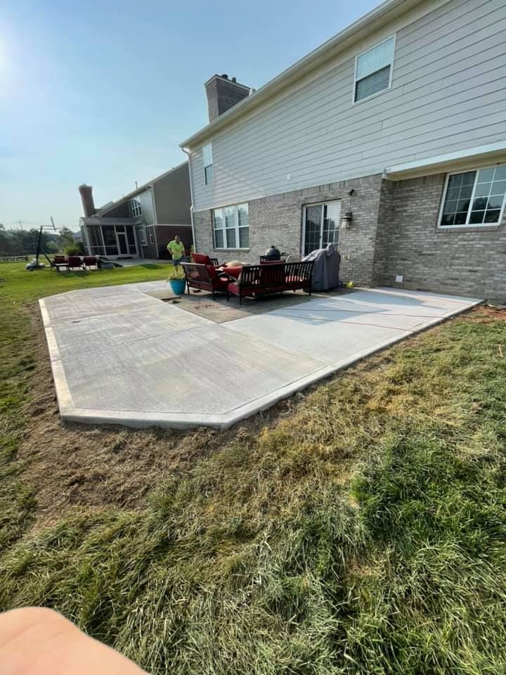 A concrete patio with a table and chairs in front of a house.