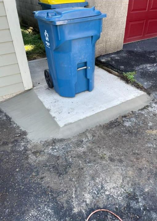 A blue trash can is sitting on a concrete curb next to a garage door.