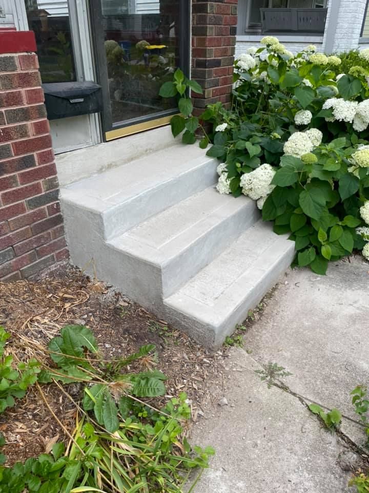 A set of concrete steps leading up to a brick building with flowers in the background.