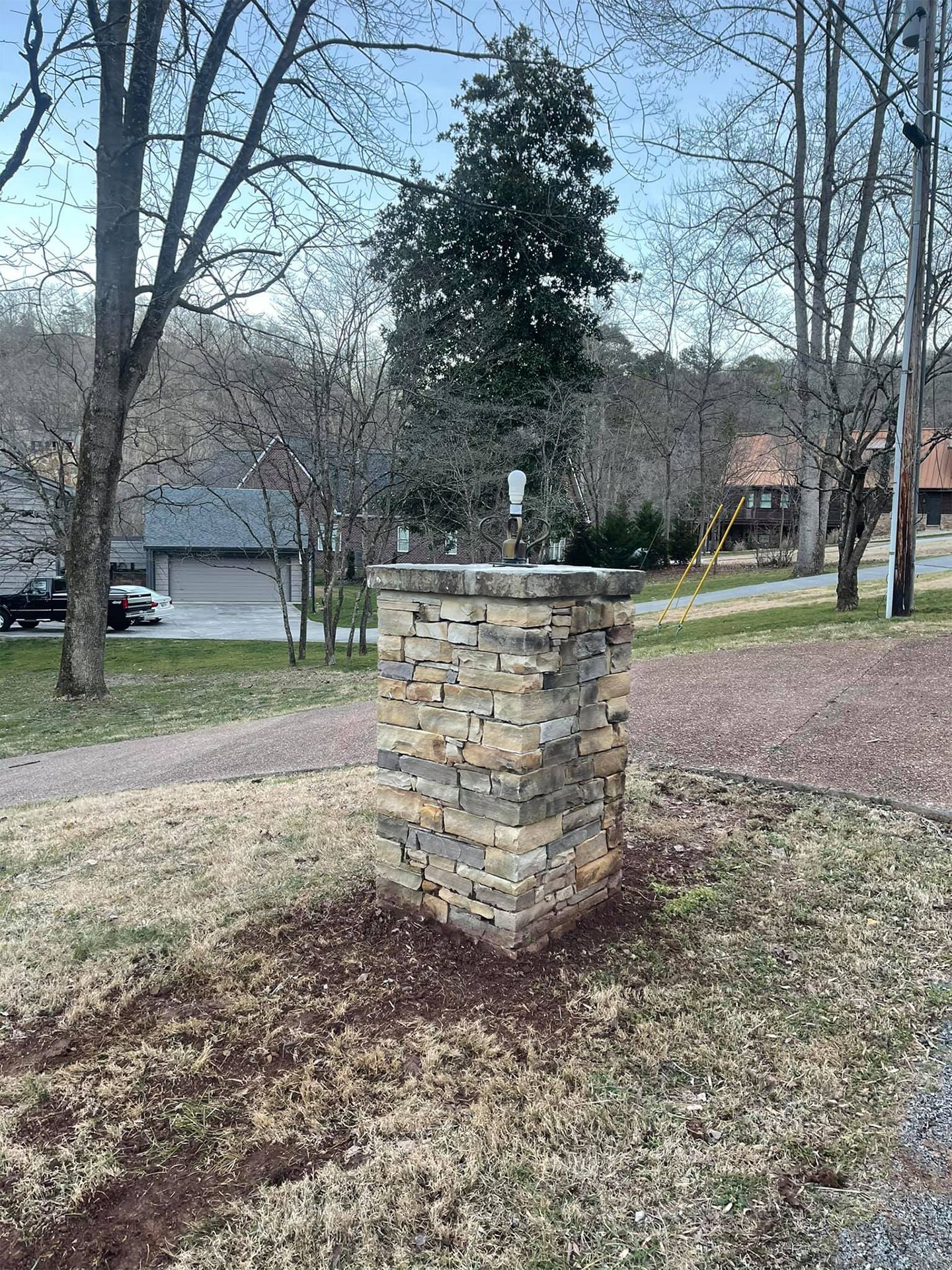 A stone pillar is sitting in the middle of a yard next to a road.