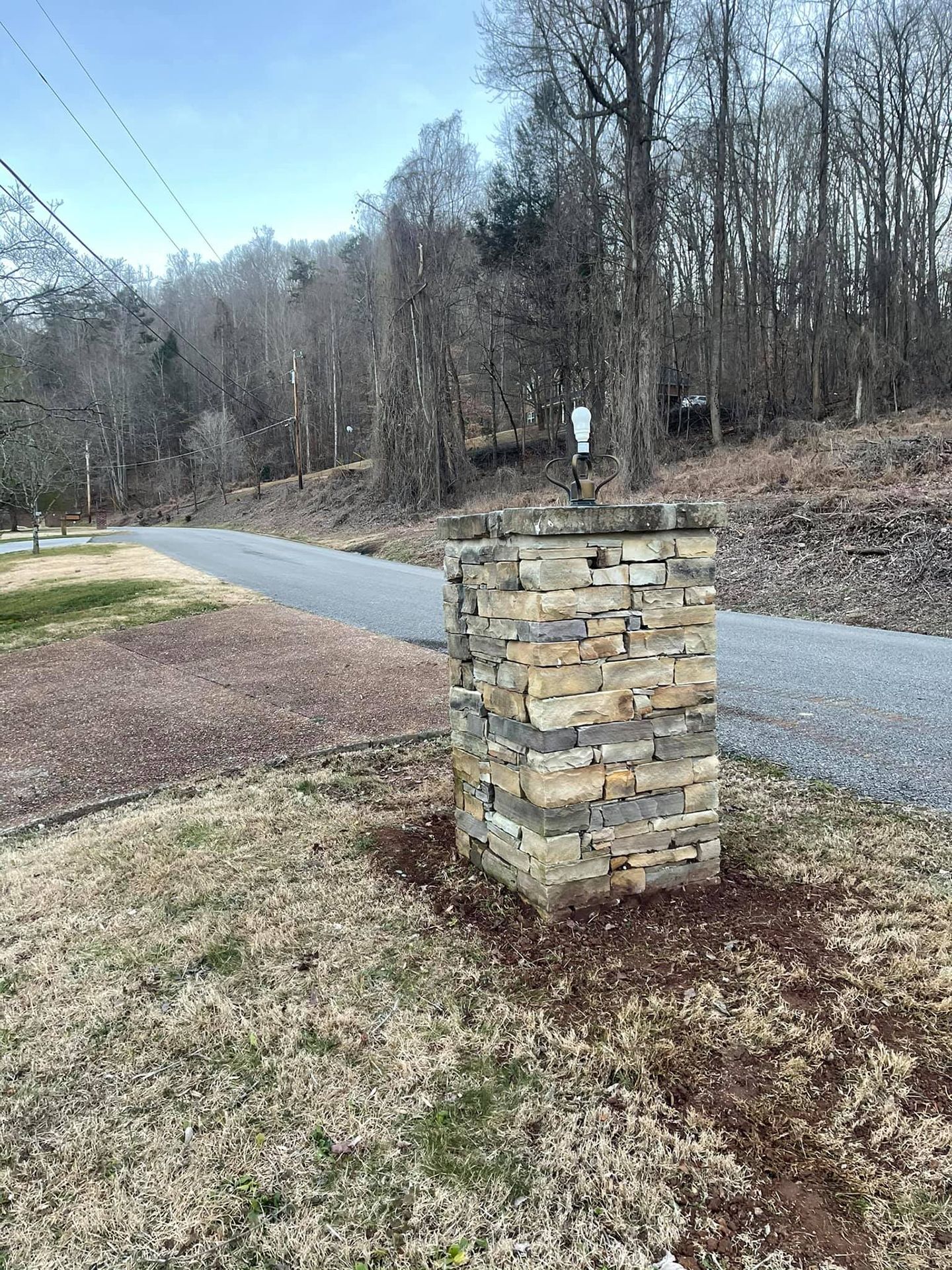A stone pillar is in the middle of a grassy field next to a road.
