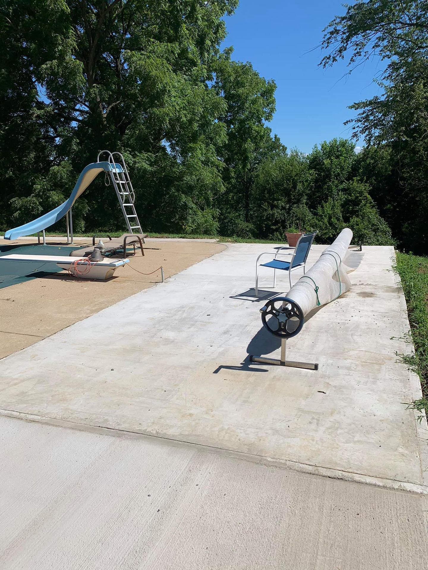 A swimming pool with a slide and chairs next to a concrete walkway.