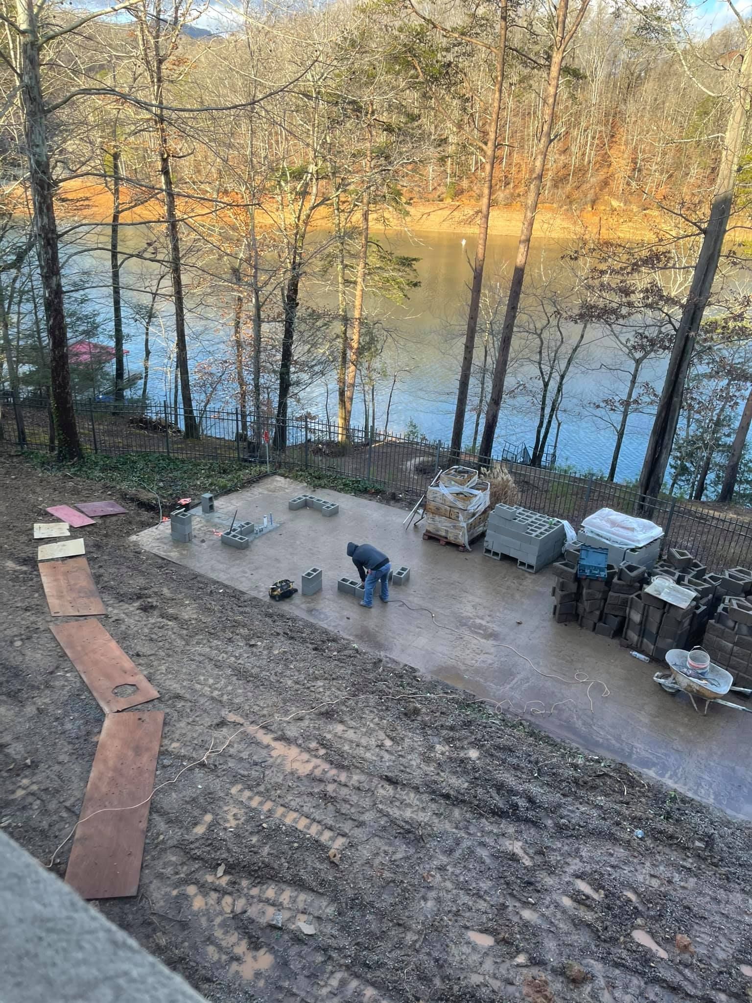 A man is working on a concrete driveway next to a lake.