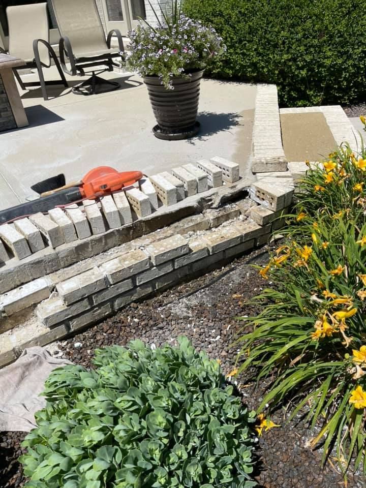 A brick wall is being built on a patio next to a potted plant.