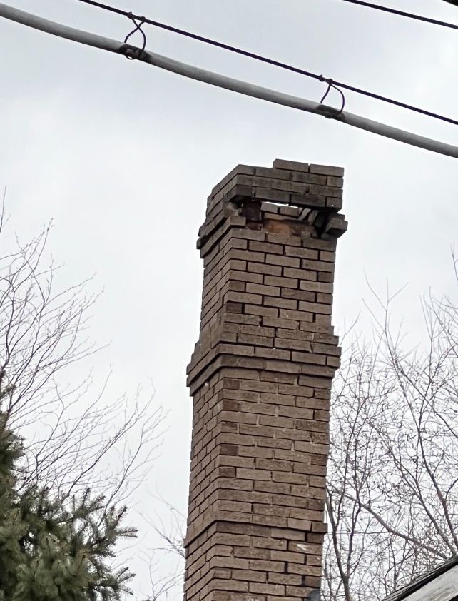 A brick chimney is surrounded by power lines against a cloudy sky