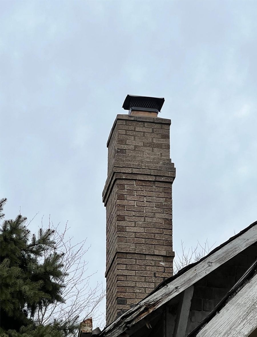 A brick chimney on top of a house with a blue sky in the background.
