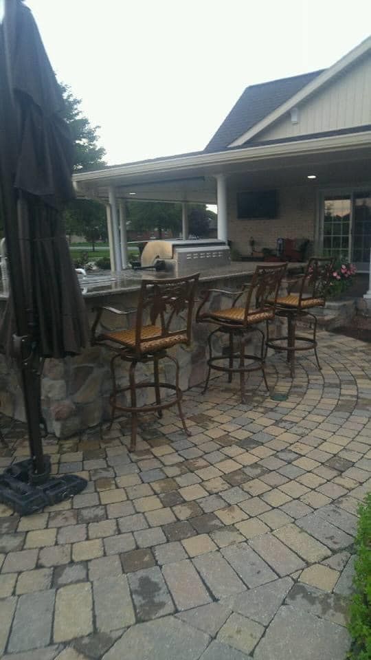 A patio with a bar and chairs and an umbrella in front of a house.